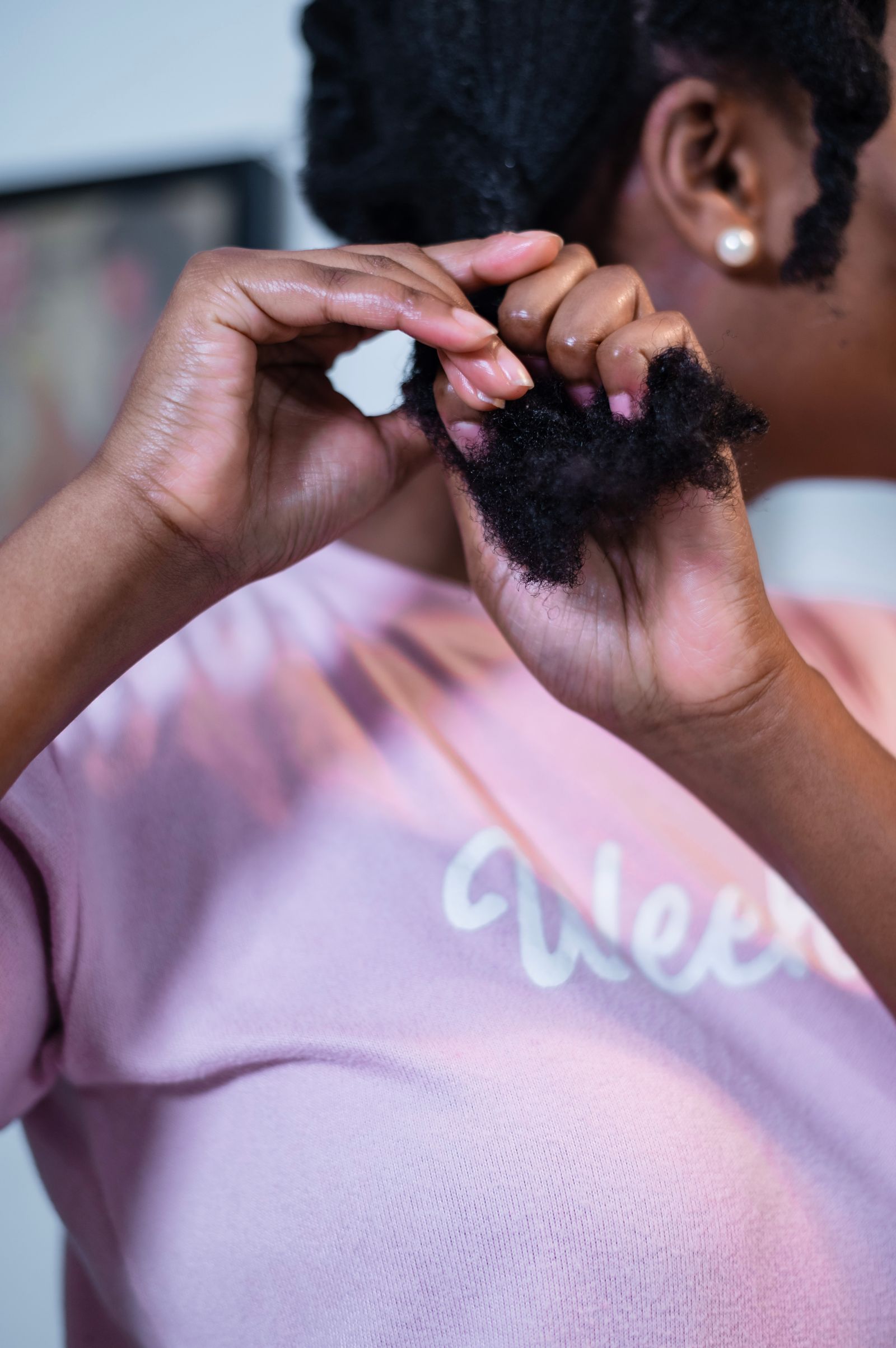 Deux mains travaillent une mèche de cheveux crépus, vues de dos au-dessus de l’épaule