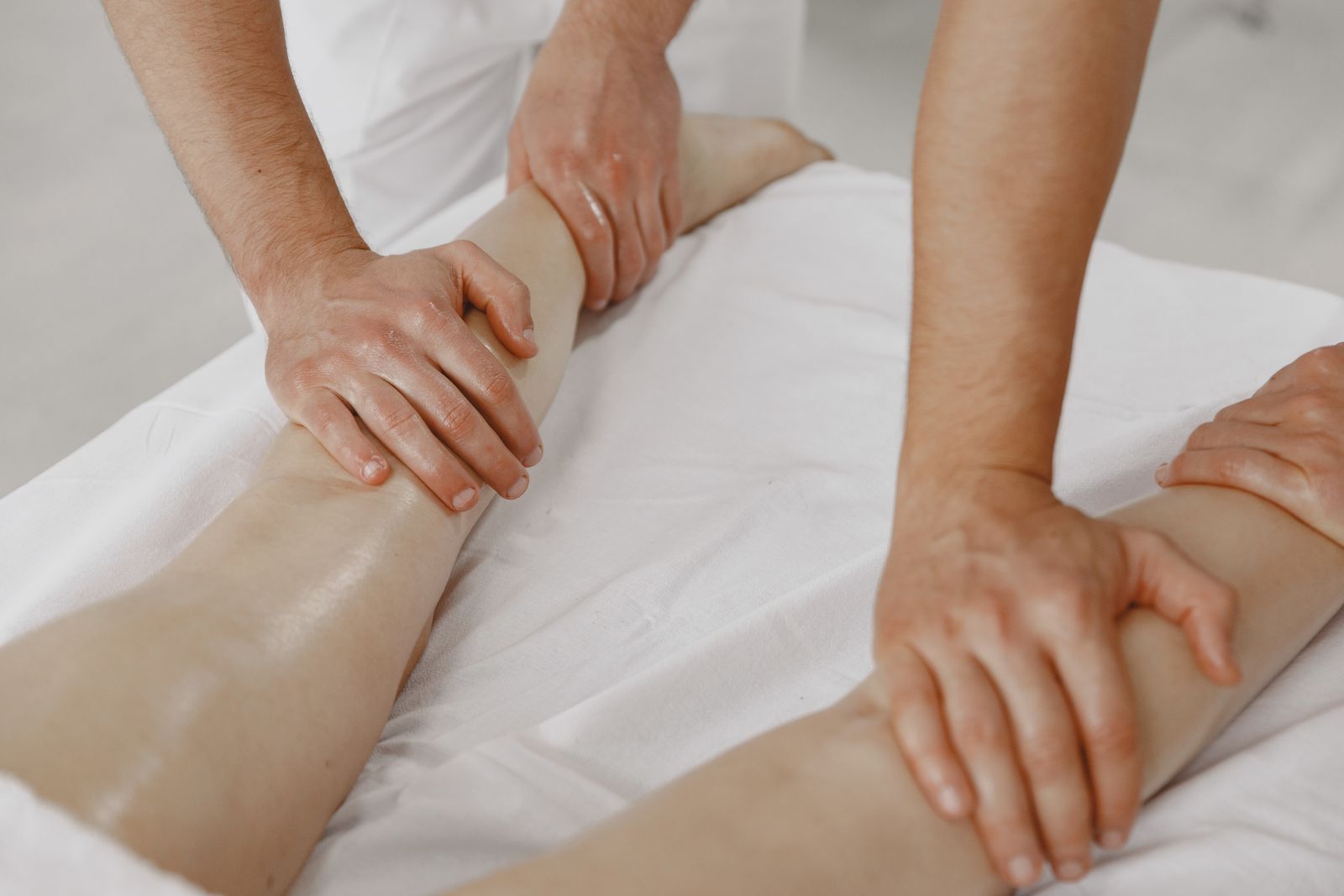 Quatre mains massent les jambes d’une personne allongée sur une table de soin recouverte de blanc