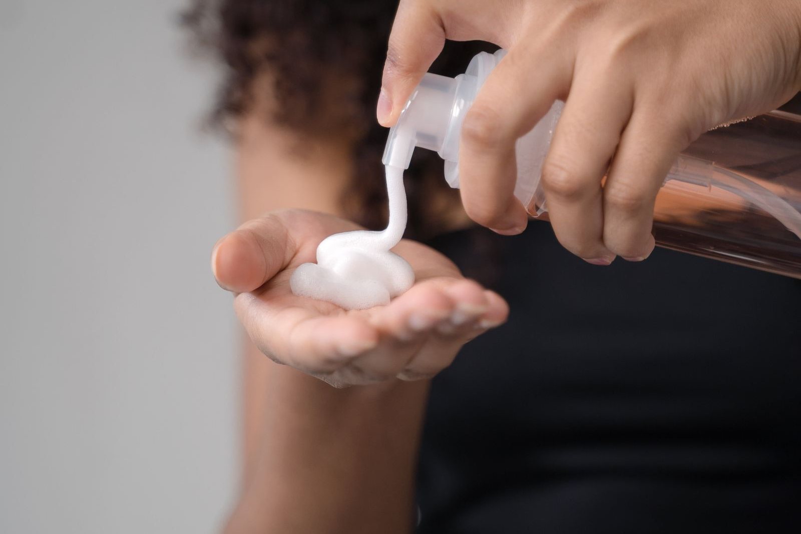 Une femme aux cheveux bouclés verse une noix de mousse coiffante blanche dans le creux de sa main à l’aide d’un flacon pompe