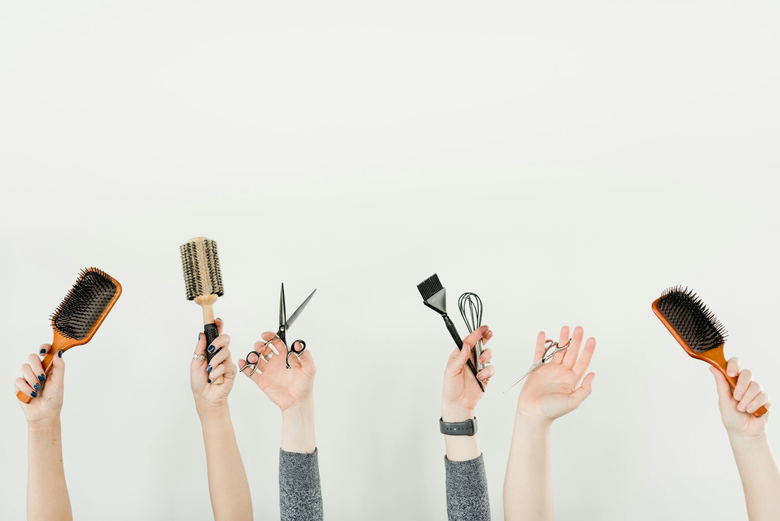 Plusieurs mains levées tenant des outils de coiffure : brosses, ciseaux, pinceau à coloration