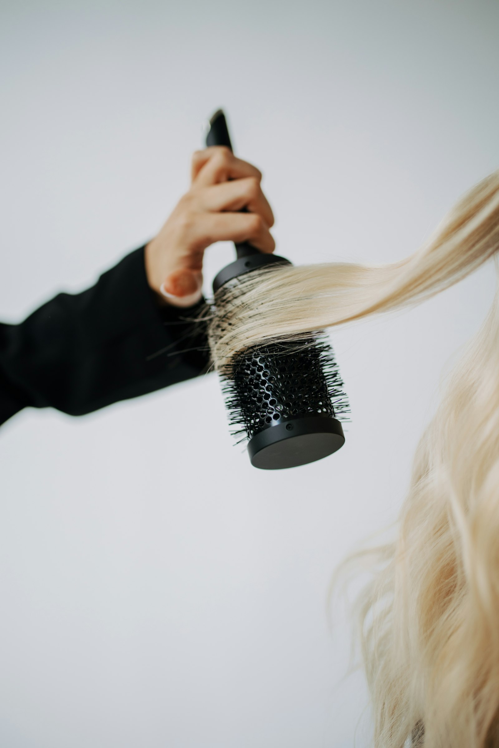 Une mèche de cheveux blonds enroulée autour d’une brosse ronde pendant un brushing