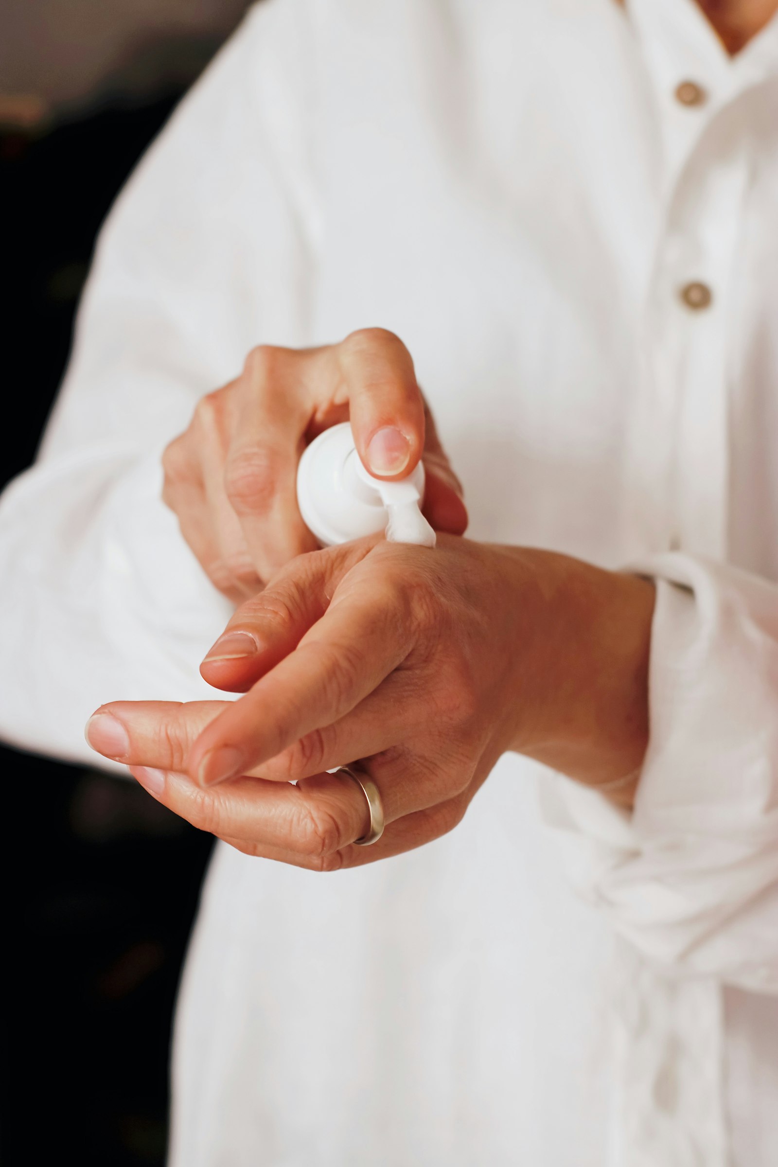 Des mains appliquent une lotion sortie d’un flacon pompe blanc