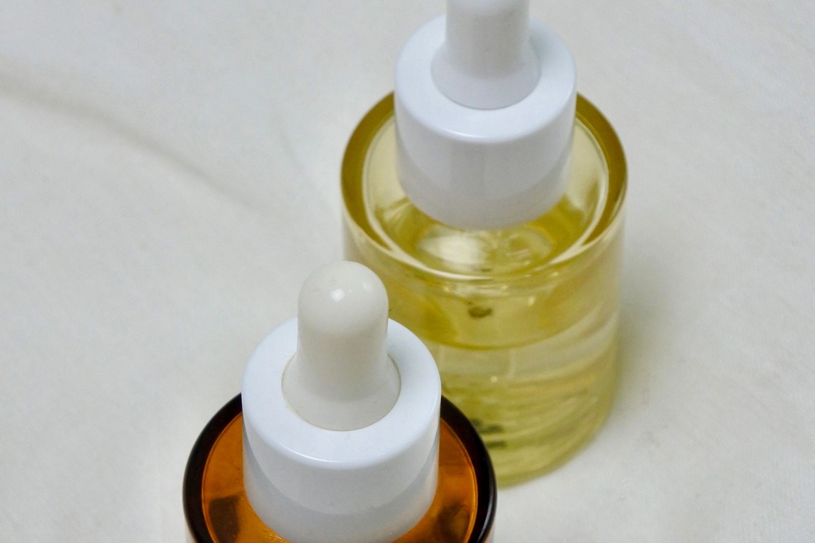Deux flacons compte-gouttes en verre, l’un ambré et l’autre jaune pâle, posés sur un tissu blanc