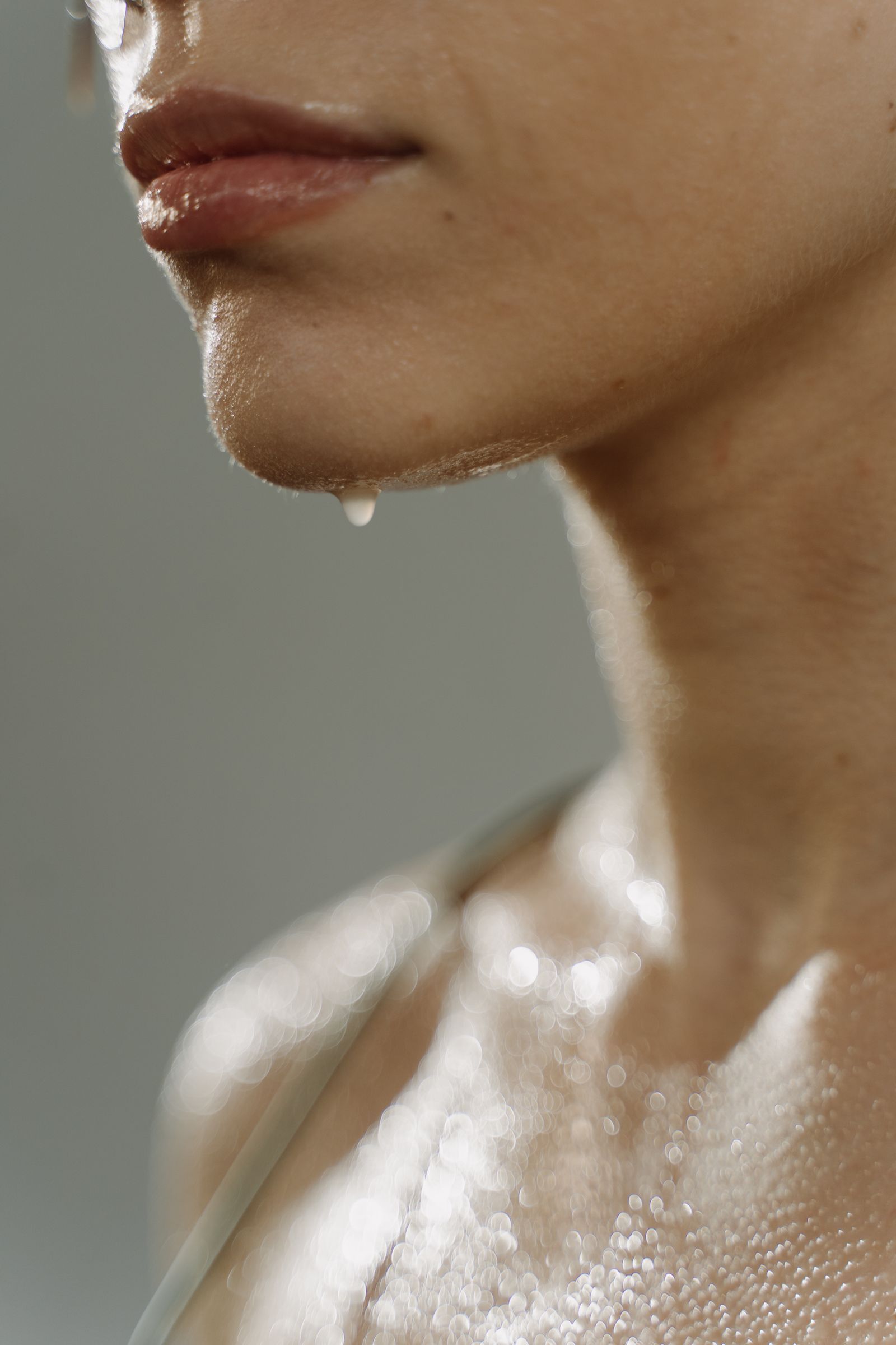 Gros plan sur un menton, un cou et un décolleté couverts de fines gouttes d’eau en contre-jour