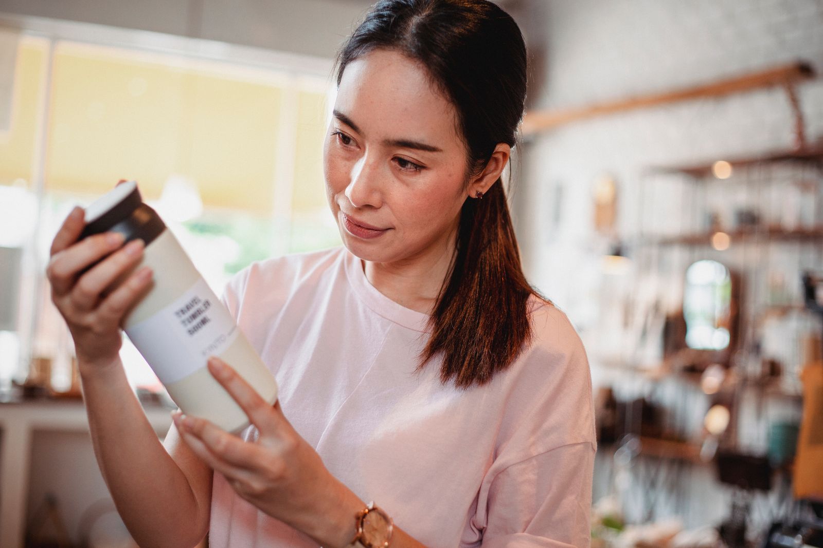 Une personne examine l’étiquette d’un flacon de soin dans une boutique, produit tenu à deux mains