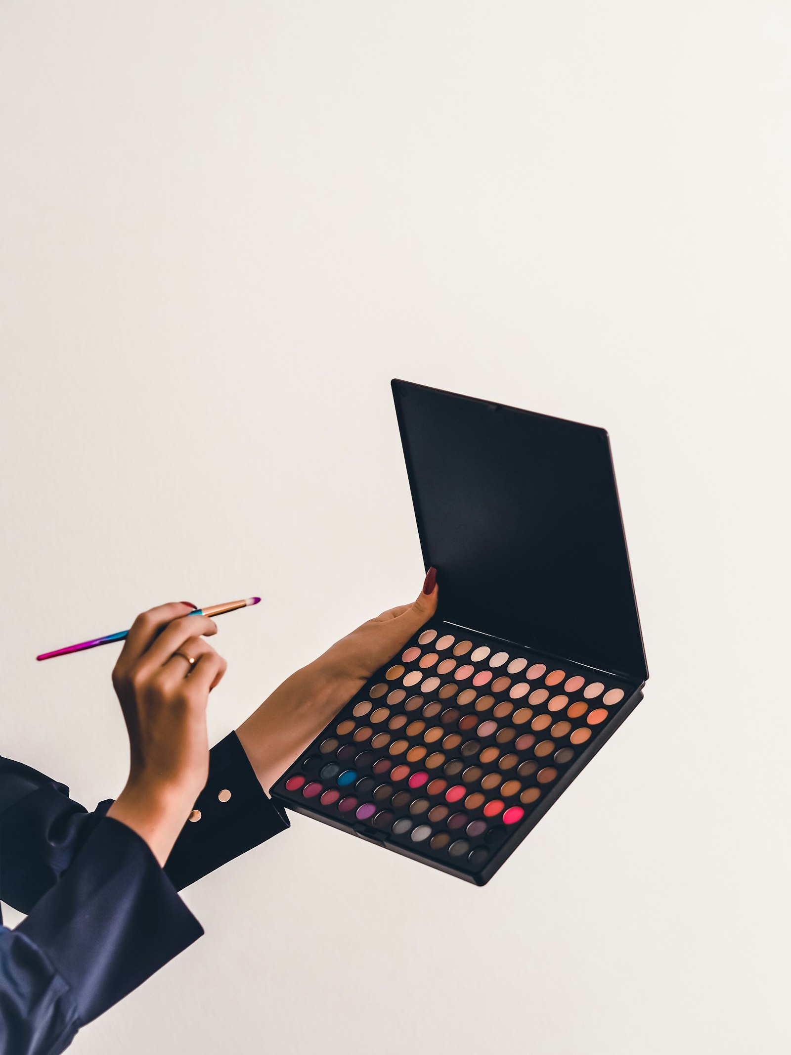 Une personne tient une palette de fards à paupières et un crayon