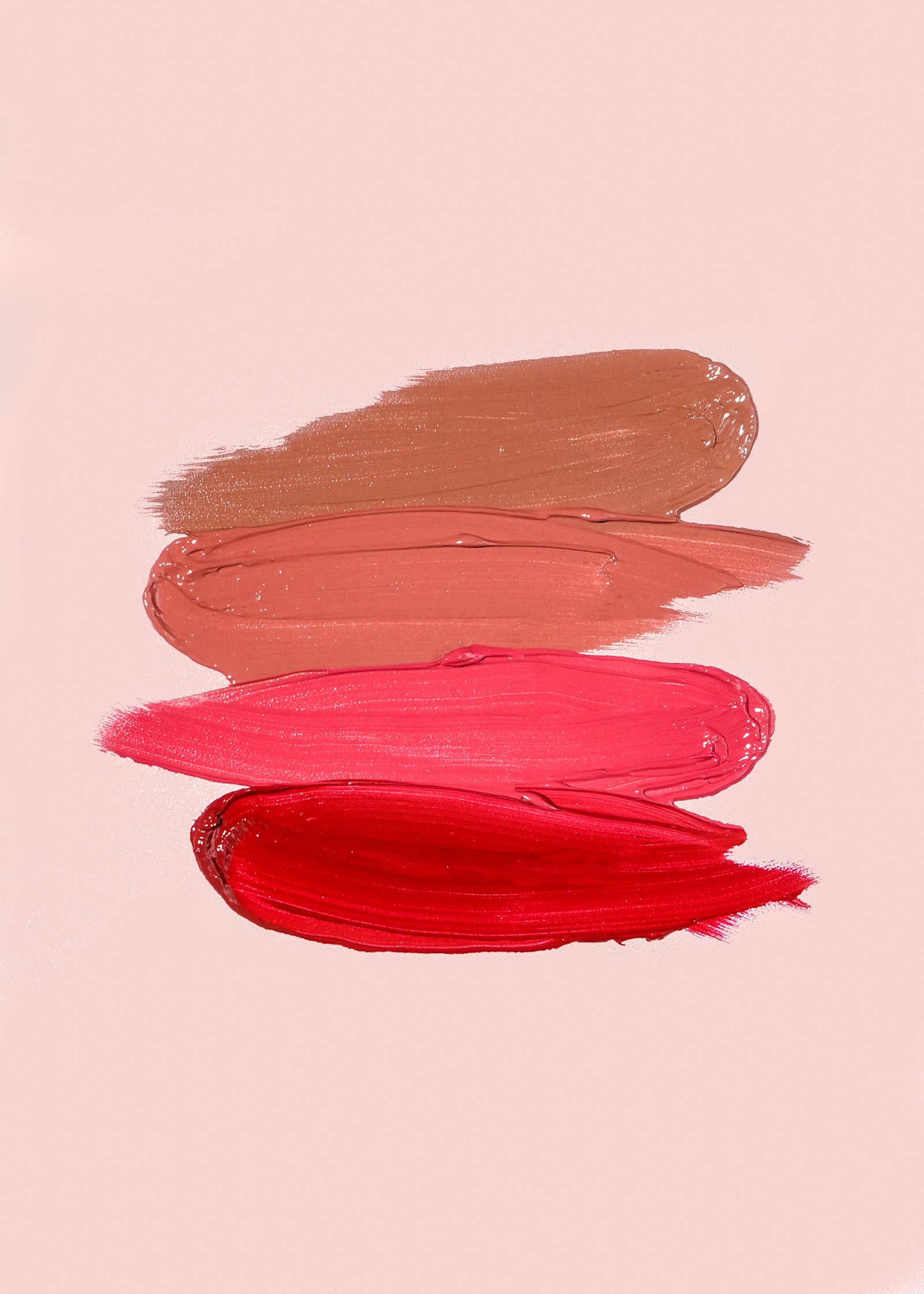 Quatre traces de rouge à lèvres, du nude au rouge vif, sur fond rose