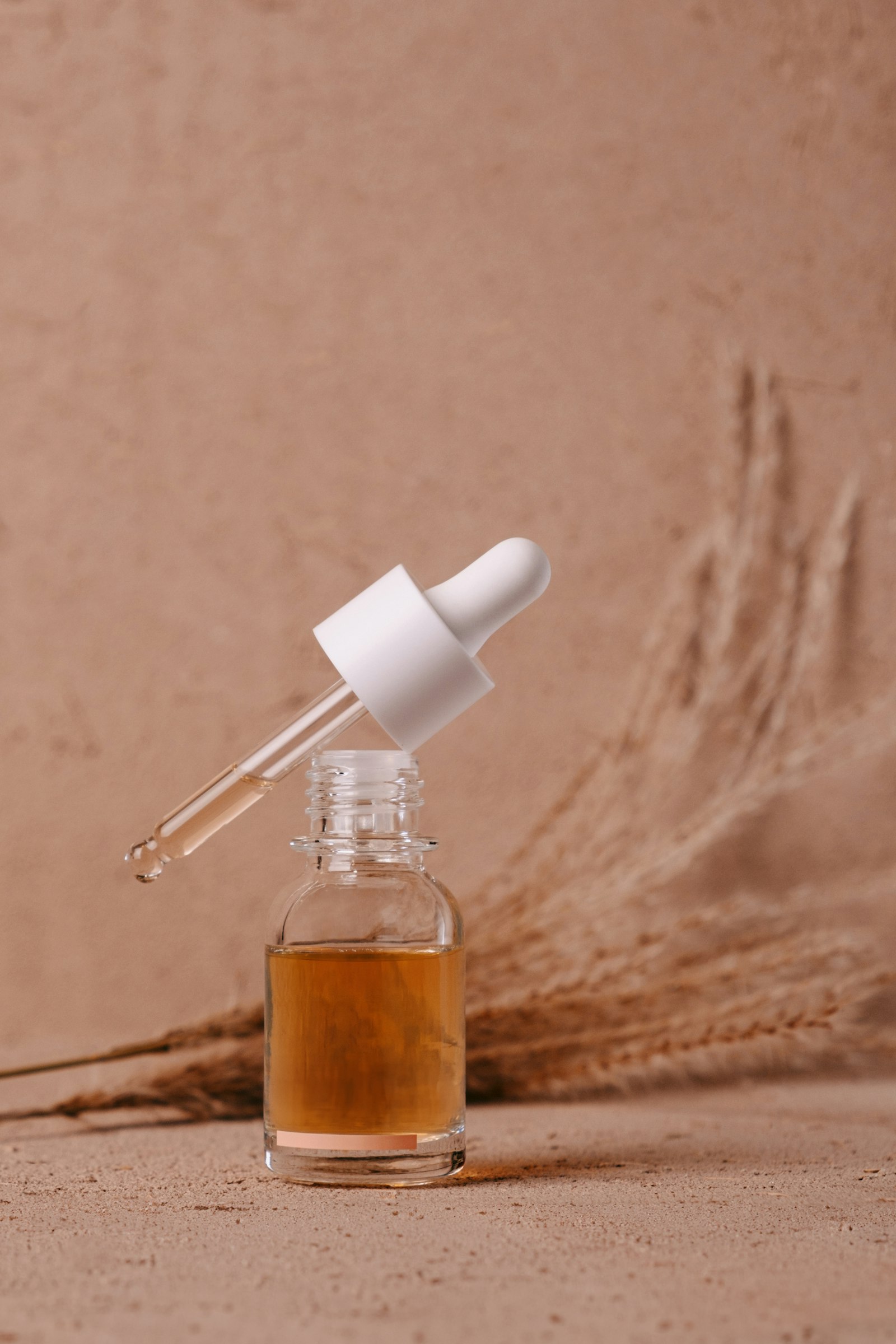 Flacon de sérum en verre et son compte-gouttes, sur un fond beige