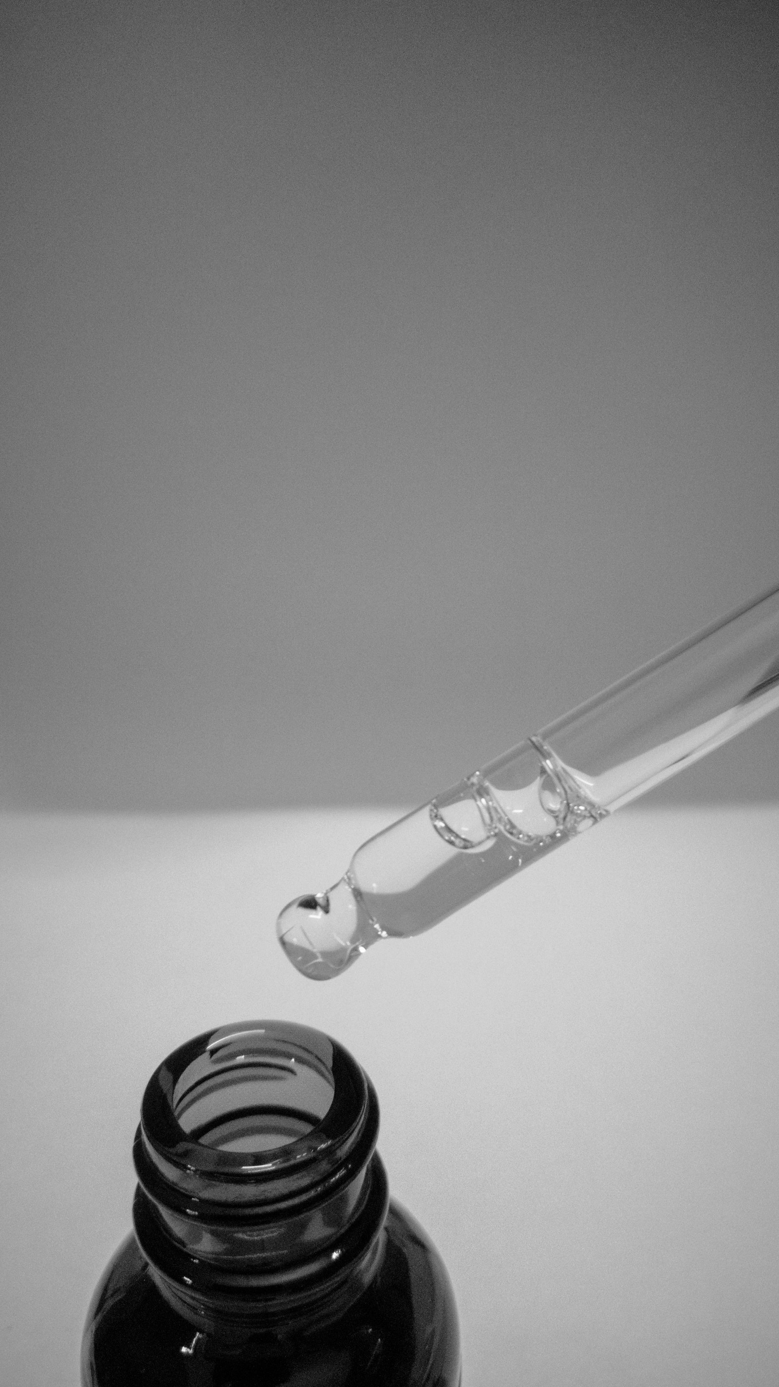 Compte-gouttes suspendu au-dessus d’un flacon de sérum, en noir et blanc