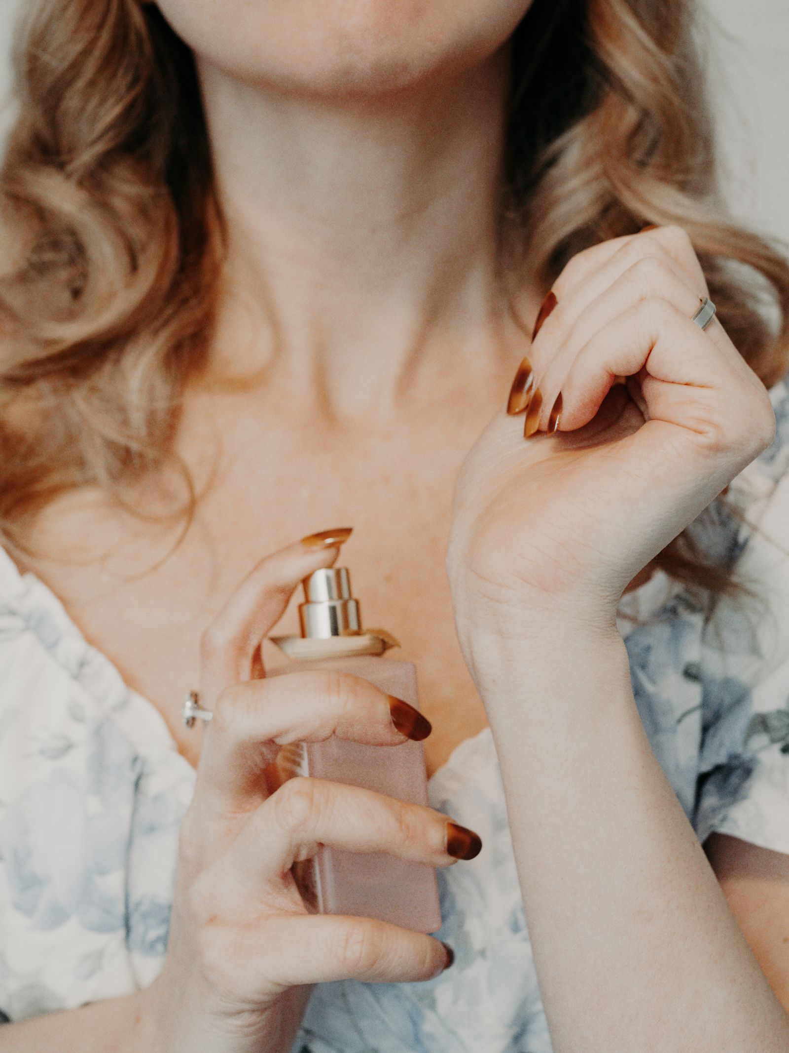 Une personne vaporise un flacon de parfum dépoli à la base du cou, poignet replié devant l’épaule
