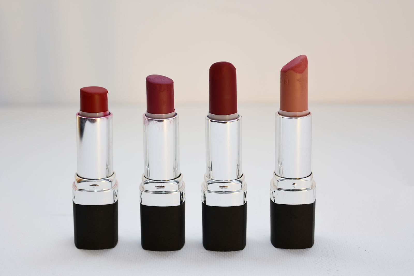 Quatre bâtons de rouge à lèvres alignés, du rouge vif au nude corail en passant par le prune