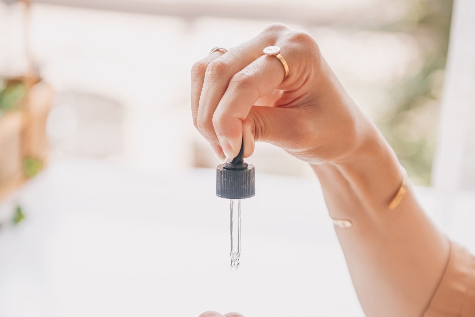 Une main tient un compte-gouttes au-dessus d’une paume ouverte, plusieurs flacons posés à côté