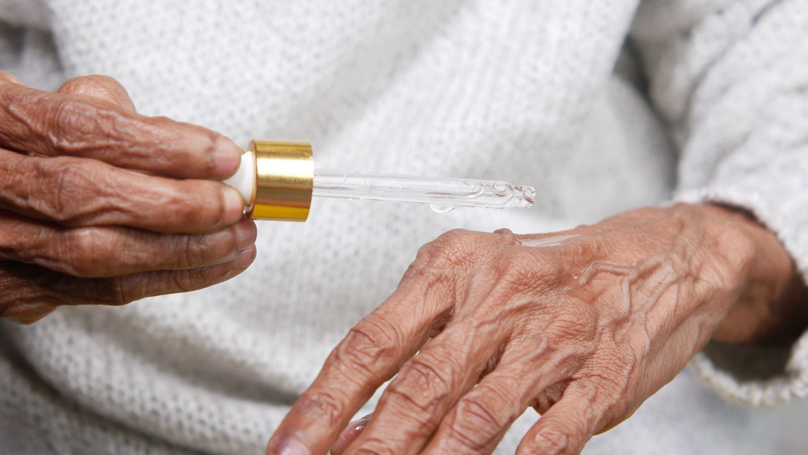 Des mains âgées déposent un sérum au compte-gouttes sur le dos de la main