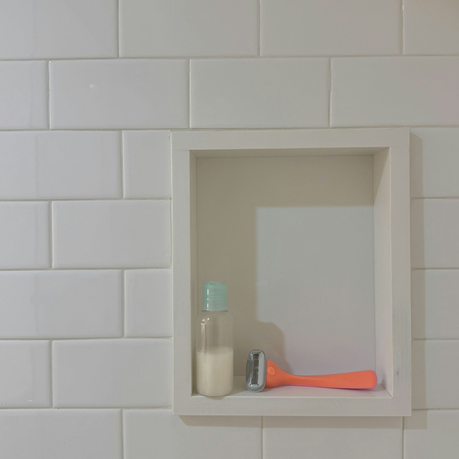 Niche de douche carrelée blanche contenant un petit flacon et un rasoir