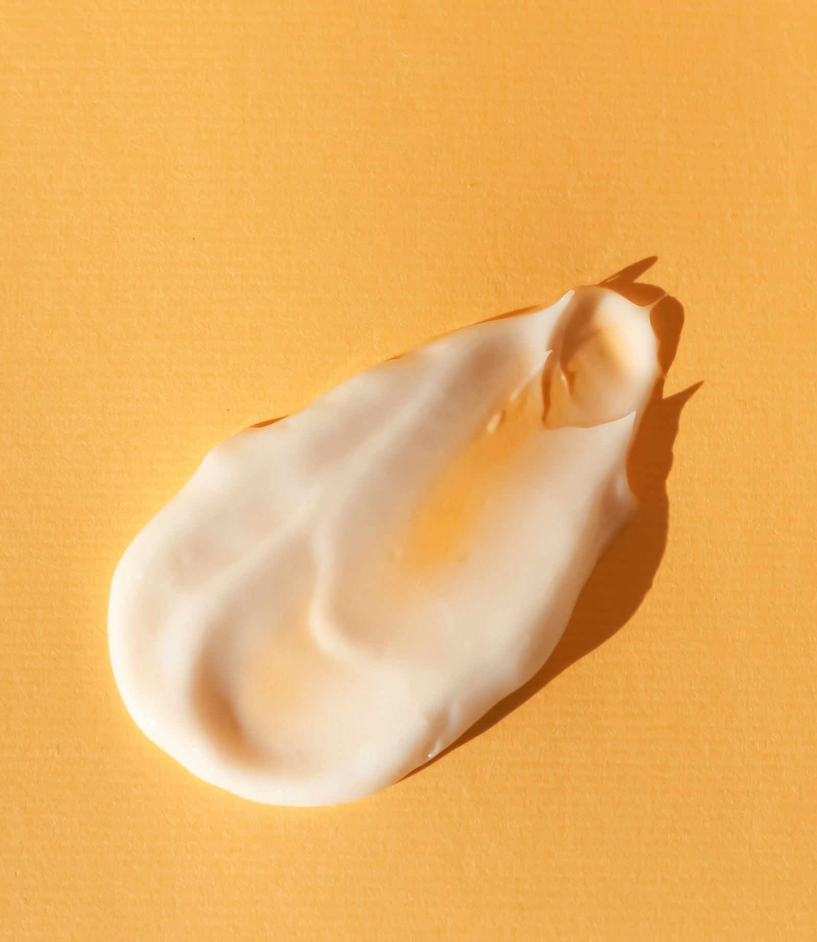 Gros plan sur une trace de crème blanche déposée sur un fond jaune
