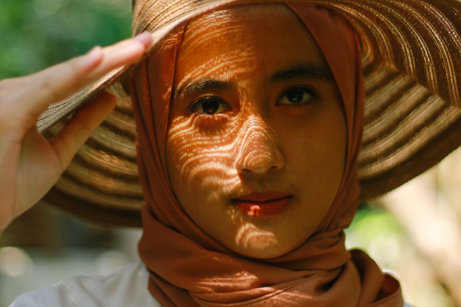 Une femme coiffée d’un chapeau de paille et d’un foulard, le visage strié par la lumière du soleil filtrée