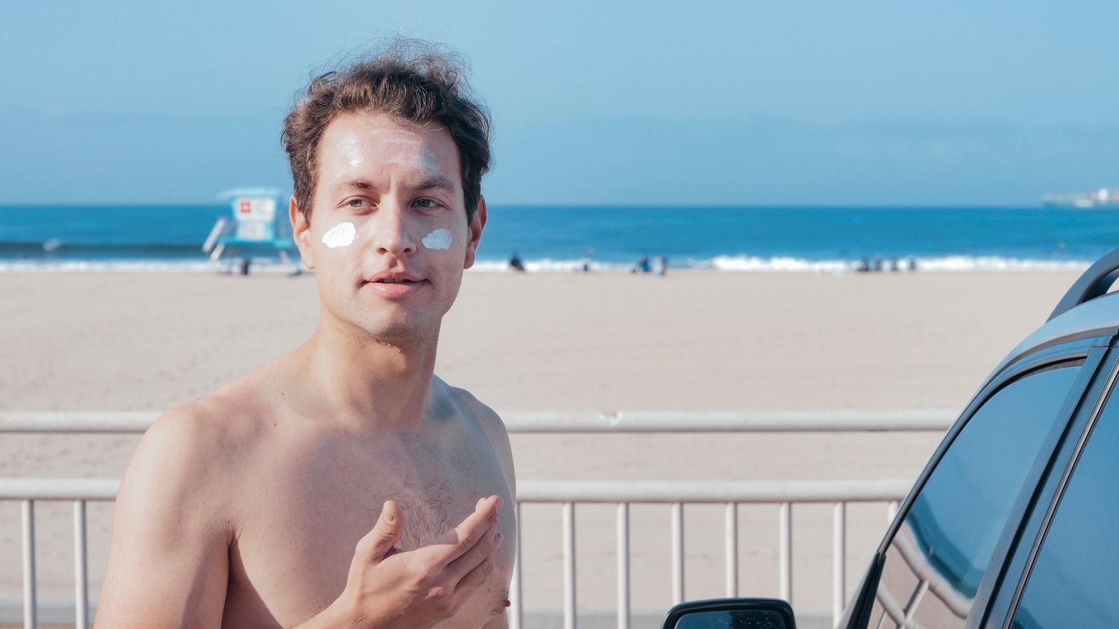 Un homme torse nu sur une plage, le front, le nez et les joues marqués de touches de crème solaire blanche encore à étaler